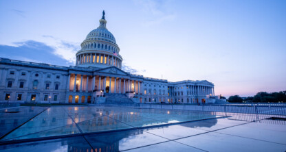 The United States Capitol building at dusk, illuminated with lights, stands under a cloudy sky with reflections on a wet surface in the foreground—an inspiring sight for those in corporate law offices nationwide.