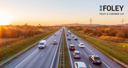 Cars and trucks drive on a divided highway at sunset, with fields and trees on both sides; Foley & Lardner LLP law offices logo appears in the upper right corner.