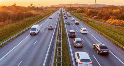 A divided highway with multiple cars and a van traveling in both directions at sunset, surrounded by grassy fields and autumn foliage—an aerial view reminiscent of the journeys lawyers in Chicago make while providing expert litigation support.
