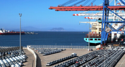 Rows of parked cars and vans near a busy shipping port with cranes, containers, and cargo ships in the background on a clear day—an industrial hub where chicago lawyers specializing in corporate law office matters might oversee transactions.