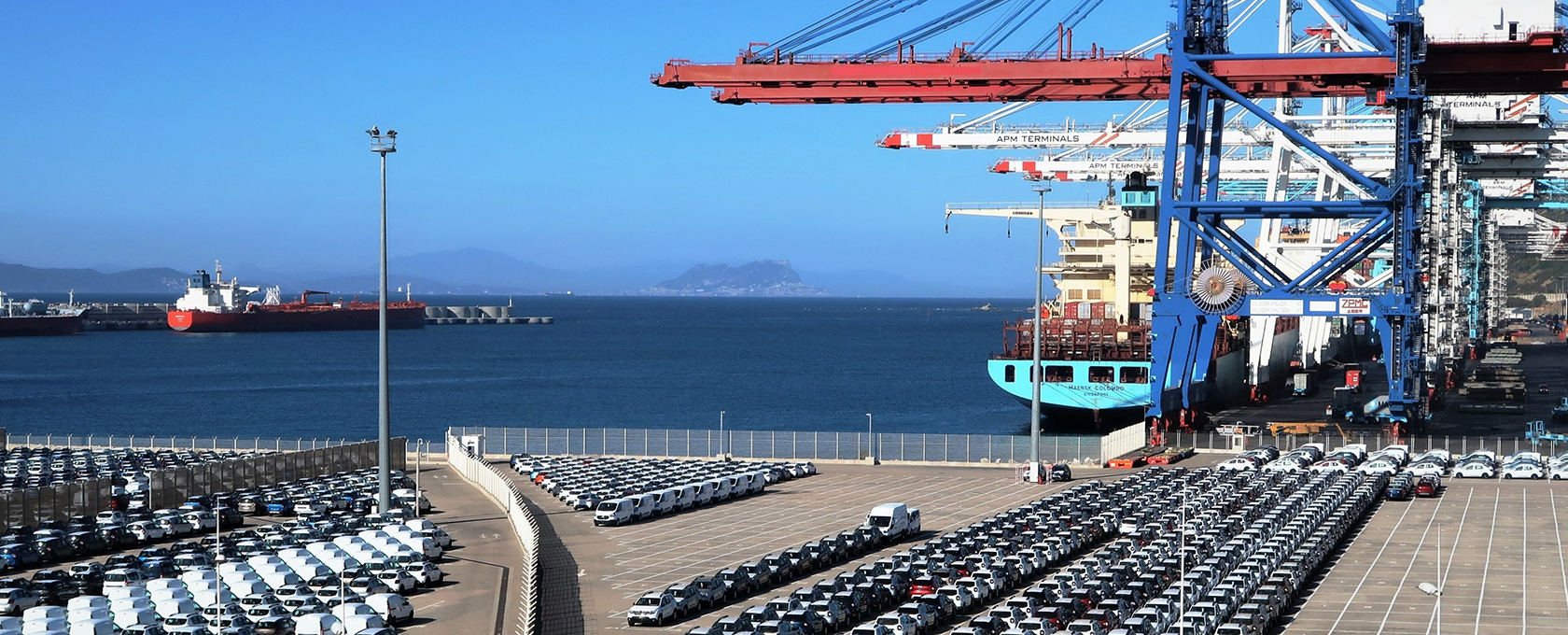 Rows of parked cars and vans near a busy shipping port with cranes, containers, and cargo ships in the background on a clear day—an industrial hub where chicago lawyers specializing in corporate law office matters might oversee transactions.