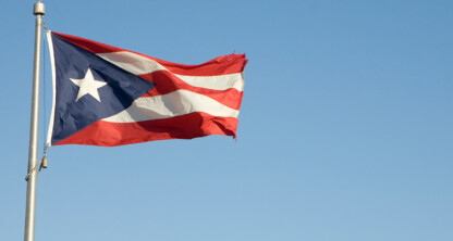 The Puerto Rican flag flies on a flagpole against a clear blue sky, just outside prominent law offices specializing in intellectual property law.