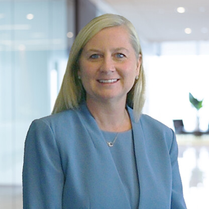 A woman with long blonde hair in a blue blazer stands in a modern corporate law office with glass walls and natural light, reflecting the dynamic environment of lawyers in Chicago.