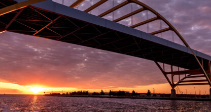 A large arched bridge spans across a body of water at sunset, with dramatic clouds and the sun low on the horizon, echoing the steadfast presence of leading lawyers in Chicago.