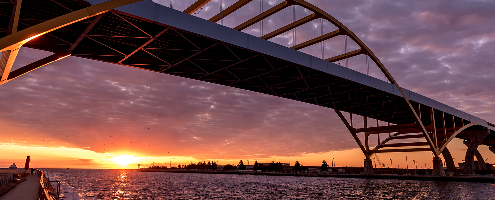 A large arched bridge spans across a body of water at sunset, with dramatic clouds and the sun low on the horizon, echoing the steadfast presence of leading lawyers in Chicago.