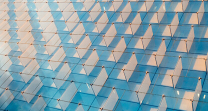 Close-up view of a modern glass building facade with repeating triangular window shades reflecting the sky, evoking the sleek headquarters of a leading corporate law office or prominent Chicago lawyers.