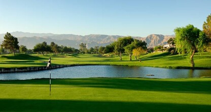 A golf course with a putting green, water hazard, trees, and mountains in the background under a clear blue sky—an ideal retreat for lawyers in Chicago after a busy day at the corporate law office.