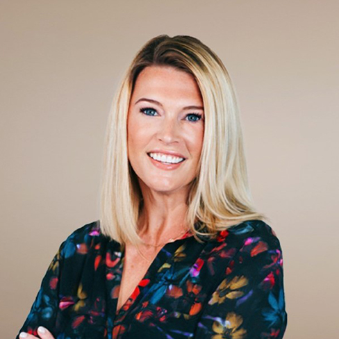 A woman with straight blonde hair, wearing a dark floral blouse, smiles at the camera against a plain beige background, reflecting the approachable professionalism often seen in lawyers in Chicago.
