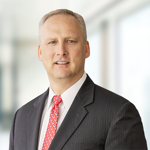 A man in a dark pinstripe suit, white shirt, and red patterned tie stands in front of a blurred indoor background, embodying the professionalism found in top Chicago lawyers and leading corporate law office environments.