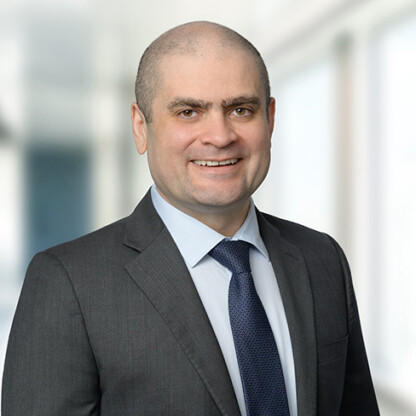 A man in a dark suit and blue tie smiles at the camera in a brightly lit corporate law office, reflecting the professionalism of lawyers in Chicago.