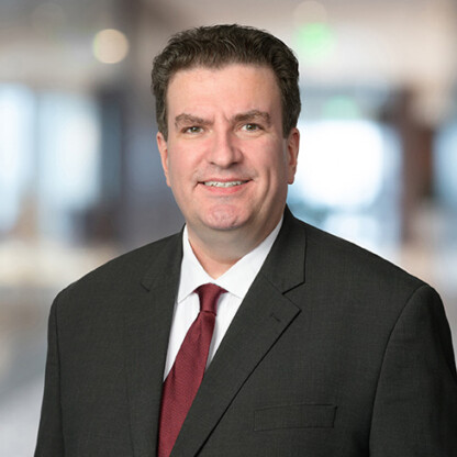 Man in a dark business suit and red tie smiles at the camera while standing in a blurred indoor office setting, representing experienced lawyers in Chicago.