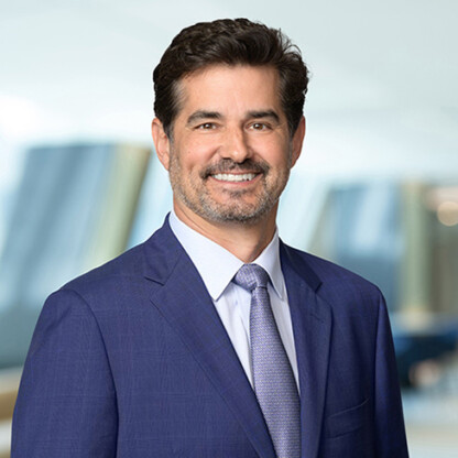 A man in a blue suit and light-colored tie smiles at the camera, standing in an office setting with blurred background—reflecting the professionalism of Chicago lawyers experienced in litigation support.