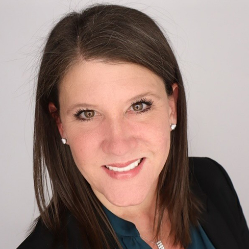A woman with straight brown hair wearing a dark blazer and teal top, smiling at the camera against a plain light background—an approachable professional in intellectual property law.