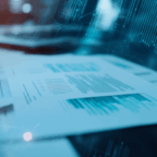 Close-up of printed documents on a desk, with a digital data overlay and a blurred background featuring a computer keyboard.