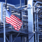 An American flag hangs on industrial metal scaffolding and piping at a manufacturing or processing facility.