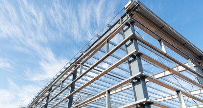Steel frame structure of a building under construction against a blue sky with scattered clouds.