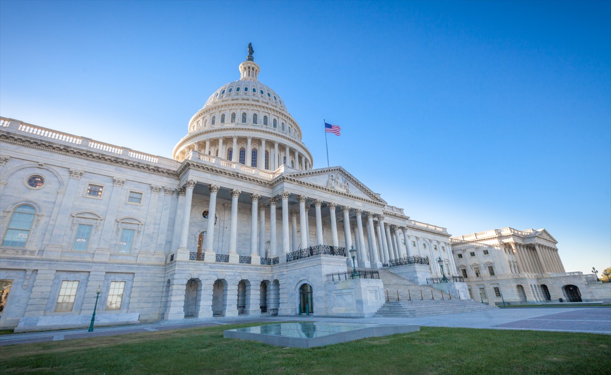 The United States Capitol building in Washington, D.C., under a clear blue sky, with the American flag flying in front.